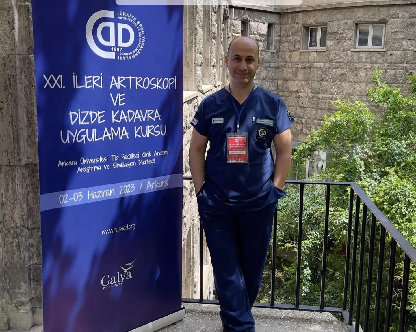 İleri artroskopi ve kadavra uygulama kursu afişinin yanında cerrahi forma giymiş hekim