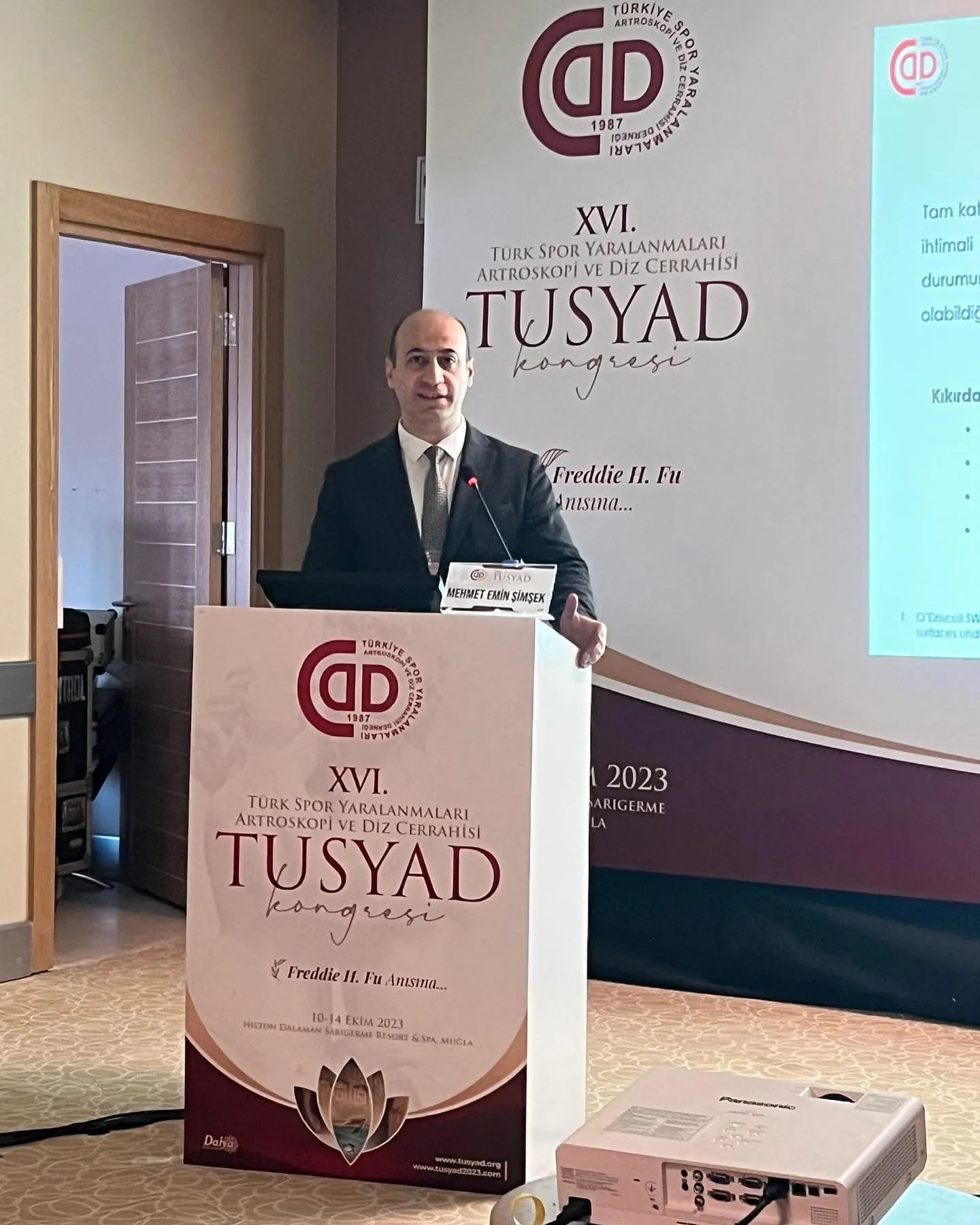Takım elbiseli hekim TUSYAD kongresi kürsüsünde bildirisini anlatırken