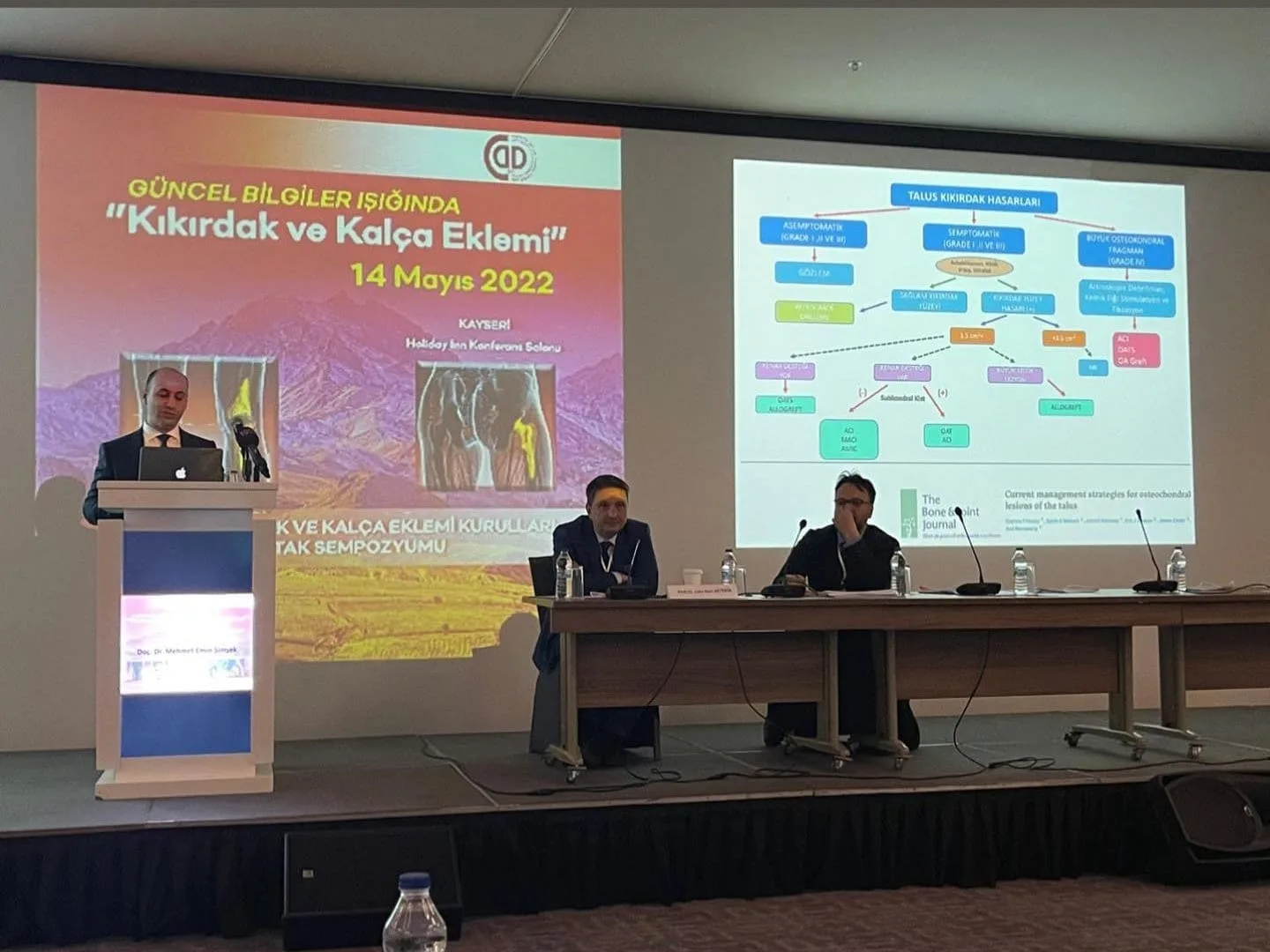 Kıkırdak ve kalça eklemi sempozyumunda kürsüde sunum yapan hekim ve arkasındaki sunum ekranı